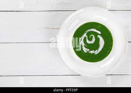 Deliziosa crema di Bright Green spinaci zuppa di broccoli con panna acida in ampio cerchio piatto sul tavolo bianco, vista da sopra, close-up Foto Stock