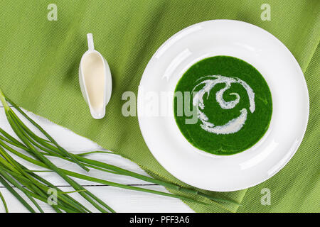 Purea di minestra di spinaci, il cipollotto, broccoli in ampio cerchio piatto sul tavolo bianco, con cipolline e crema su sfondo, vista da ab Foto Stock