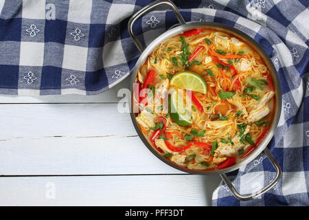 Thai piccante pollo al curry di spessore e favorire la zuppa di noodle con latte di cocco, le verdure e le erbe in un recipiente di cottura sul tavolo di legno e tradizionale ricetta asiatica, Foto Stock