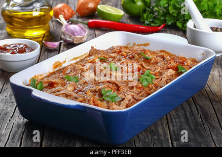 Shredded carne di pollo saltati in salsa barbecue, caricato con smoky chipotle sapori in una teglia, sul vecchio tavolo in legno con ingredienti sullo sfondo Foto Stock