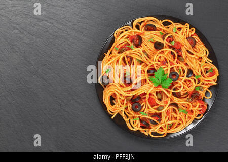 Delizioso Spaghetti alla puttanesca con capperi. olive, acciughe, la salsa di pomodoro cosparsa di prezzemolo sulla piastra nera sul vassoio di pietra, autentico basic Foto Stock