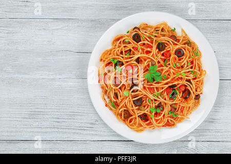 Delizioso Spaghetti con capperi. olive, acciughe, la salsa di pomodoro cosparsa di prezzemolo sulla piastra bianca sul tavolo di legno, autentica ricetta di base vista f Foto Stock