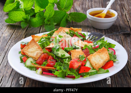 Deliziosi piatti tradizionali Fattoush o insalata di pane con crostoni di pane pita, cetriolo, pomodoro, lattuga e erbe su piastra bianca. di menta fresca e olio, limone, sommacco Foto Stock