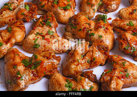 Materie succosa di ali di pollo marinato con il miele, la salsa di soia, spezie e spolverate con del prezzemolo tritato finemente sul tavolo bianco, preparato per arrosti, asian ri Foto Stock