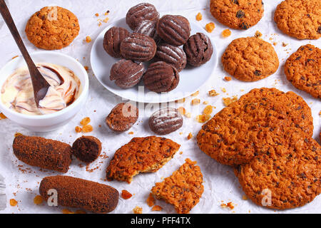 Cioccolato artigianale chip cookie di fiocchi d'avena, uvetta biscotti al cioccolato, noci e yogurt fresco in un recipiente su un foglio di carta sul tavolo di legno, vista da sopra, vicino- Foto Stock