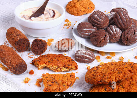 Cioccolato artigianale chip cookie di fiocchi d'avena, uvetta biscotti al cioccolato, noci e yogurt fresco in un recipiente su un foglio di carta sul tavolo di legno, vista da sopra, vicino- Foto Stock