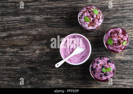 Sana deliziosi dessert estivo di ribes nero decorato con foglie di menta in bicchieri di vetro sul vecchio legno scuro tabella, congelate Panna ricotta Yogur Foto Stock