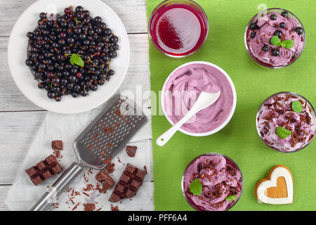 Ribes nero su piastra, layered gelato dessert berry decorato con foglie di menta e spolverati con scaglie di cioccolato in bicchieri di vetro, ingredienti e h Foto Stock