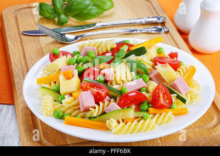 Luce colorata sano antipasto insalata di pasta italiana fusilli con la carota e la zucchina bastoni, prosciutto, formaggio, piselli verdi, pomodori ciliegia su bianco pla Foto Stock