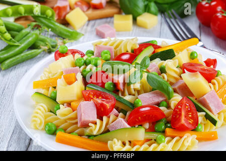 Luce colorata sano antipasto insalata di pasta italiana fusilli con la carota e la zucchina bastoni, prosciutto, formaggio, piselli verdi, pomodori ciliegia su bianco pla Foto Stock
