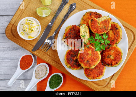 Freschi e deliziosi fritte fatte in casa Torte Pesce sulla piastra bianca sul tagliere con la forcella, coltello, e salsa di spezie, ricetta classica, vista da sopra, vicino-u Foto Stock