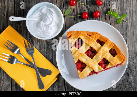 Fetta di deliziosa casa di ciliege acide pie sulla piastra. Ciotola con panna, dessert forche su legno scuro, tavola ricetta classica, vista da sopra Foto Stock