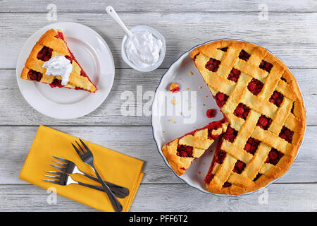 Fetta di deliziosa casa di ciliege acide pie sulla piastra. Ciotola con panna, dessert forcelle e tutta la torta sul tavolo di legno, ricetta classica, vista dal Foto Stock