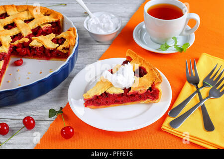 Fetta di deliziosa casa di ciliege acide pie sulla piastra. Ciotola con panna, dessert forcelle e tart tagliato a fettine e la tazza di tè sul tavolo di legno, cl Foto Stock