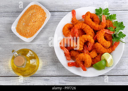 Luce e croccante fritti croccanti code di gamberi sulla piastra bianca sul tavolo di legno con il pangrattato e una bottiglia di olio di oliva, vista da sopra Foto Stock