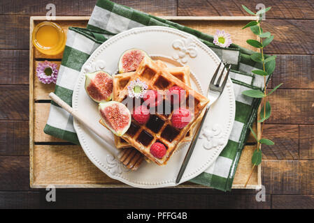 Cialde belghe con fichi, lamponi e miele in legno che serve vassoio. Vista superiore della gustosa prima colazione Foto Stock