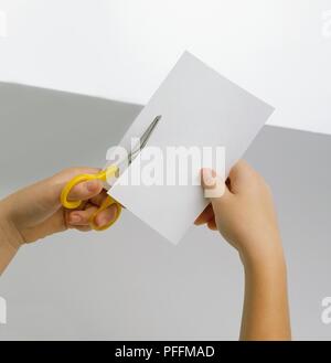 La mano della bambina striscia di taglio dal pezzo di carta bianca, close-up Foto Stock