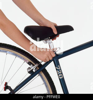 Ragazza con le mani in mano la regolazione in altezza di una sella per bicicletta con una chiave per viti a testa esagonale incassata, close-up Foto Stock