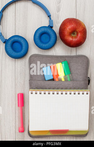 Forniture scolastiche. Aprire il quaderno sul sacchetto custodia a matita con colore pennarelli e marker, cuffie e apple rosso grigio su tavole di legno. Vista superiore con Foto Stock