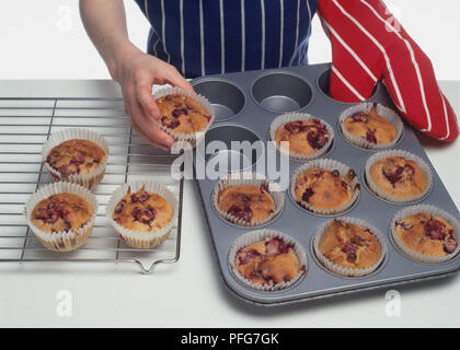 Cotta lampone muffin essendo presi al di fuori del vassoio da forno e posto sulla griglia di raffreddamento Foto Stock