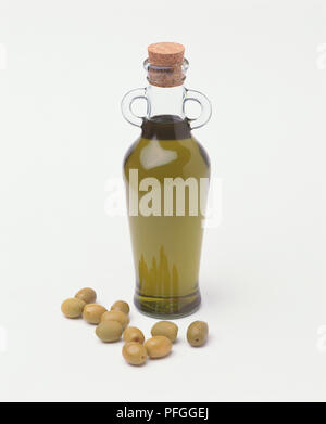 Bottiglia di olio d'oliva circondato da olive verdi. Foto Stock