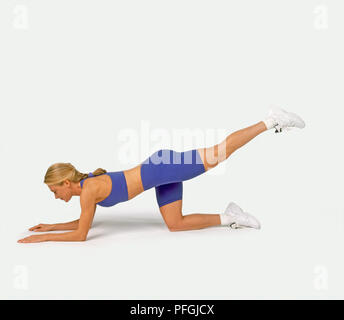 Donna in palestra suit inginocchiato avanti mentre si estende la gamba dritta dietro di lei Foto Stock
