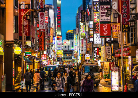Strada trafficata in notturna a Shinjuku, Tokyo, Giappone, con molti segni al neon in giapponese Foto Stock
