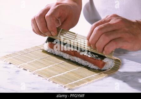 Contenente il sushi nori alghe, riso e tonno, essendo arrotolato a mano all'interno di bamboo mat, close-up Foto Stock