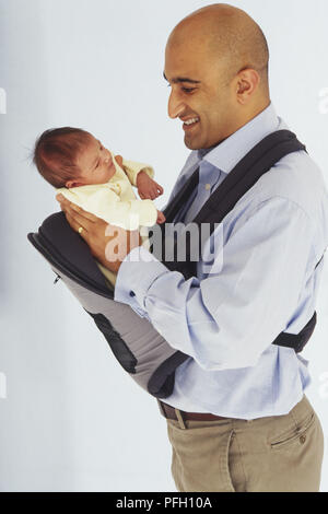 Sorridente, rasato con testa di uomo con baby girl in baby sling, vista laterale Foto Stock