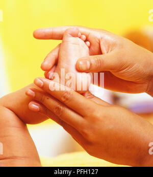 Donna di massaggio mani bambina il piede, close-up Foto Stock