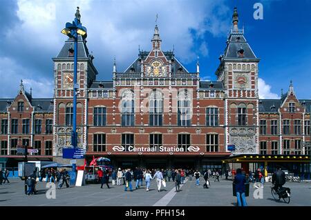 Paesi Bassi, Amsterdam Centraal Station, del tardo XIX secolo facciata, con pedoni sul piazzale della stazione, vista frontale Foto Stock