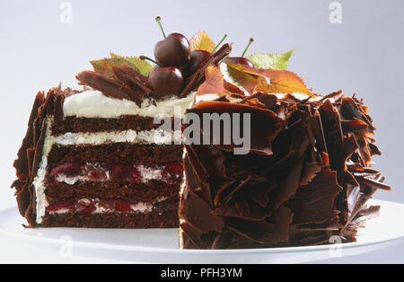 Torta al cioccolato guarnita con crema bianca, ciliegie fresche e foglie di autunno, lati rivestiti con i riccioli di cioccolato e la sezione rimossa per rivelare sezione, vista laterale Foto Stock