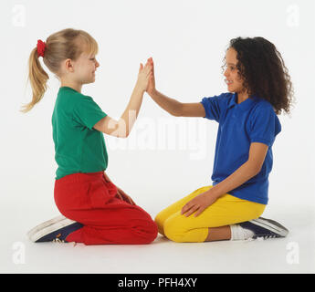 Due ragazze in abiti colorati seduto sulle ginocchia e battimani reciprocamente le mani Foto Stock