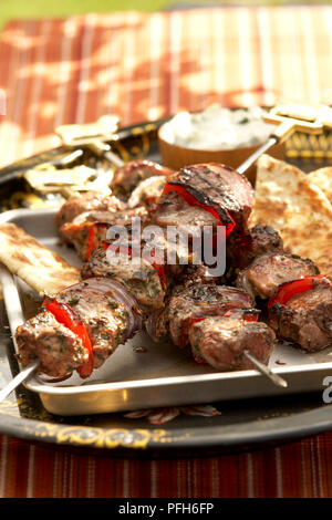 Agnello shish kebab, cipolle e peperoni rossi su spiedini, servita con pane pitta e salsa di yogurt Foto Stock