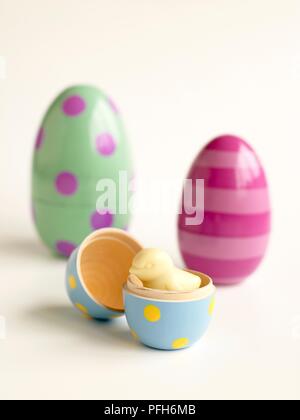 Il cioccolato bianco chick all'interno del giocattolo dipinte di uovo, due dipinti uova giocattolo in background, close-up Foto Stock