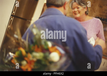 Vista posteriore dell'uomo azienda mazzo di fiori dietro la schiena, Donna sorridente in piedi di fronte Foto Stock