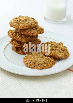 Farina di avena cookie su piastra, bicchiere di latte in background, close-up Foto Stock