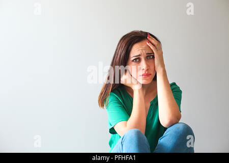 Ritratto di una donna triste guardando pensieroso circa i suoi problemi di fronte a un muro grigio Foto Stock