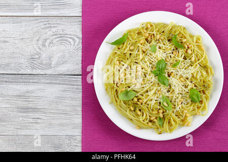 Bucatini italiana - spaghetti con sugo di basilico Pesto, spruzzata con pinoli e parmigiano grattugiato e decorate con foglie di basilico sulla piastra bianca Foto Stock