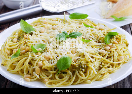 Gustosi bucatini italiana - spaghetti con sugo di basilico Pesto, spruzzata con pinoli e parmigiano grattugiato sulla piastra bianca su assi di legno, ingre Foto Stock