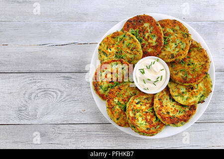 Deliziosi piatti cotti in forno frittelle di zucchine su piastra bianca con panna acida nel centro del piatto spolverati con un trito di erba cipollina, sana e facile vege Foto Stock