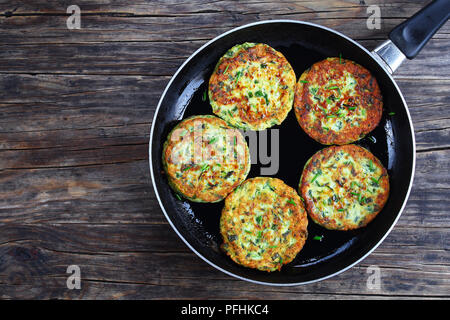 Deliziose frittelle di zucchine cosparso con un trito di erba cipollina in padella, sul vecchio legno scuro tavolo, ricetta vegetariana, vista da sopra Foto Stock