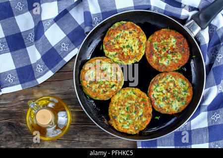 Deliziose frittelle di zucchine cosparso con un trito di erba cipollina in padella, sul vecchio dark tavolo in legno con asciugamano da cucina vegetariana ricetta, vista dal Foto Stock