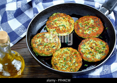 Deliziose frittelle di zucchine cosparso con un trito di erba cipollina in padella, sul vecchio dark tavolo in legno con asciugamano da cucina vegetariana ricetta, vista dal Foto Stock