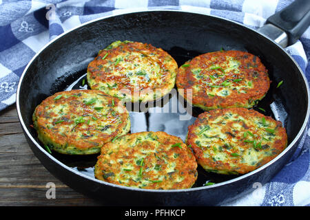 Deliziose frittelle di zucchine cosparso con un trito di erba cipollina in padella, sul vecchio dark tavolo in legno con asciugamano da cucina vegetariana ricetta, close-up Foto Stock