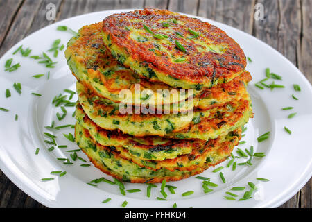 Croccanti frittelle di zucchine cosparso con un trito di erba cipollina sul piatto da portata, sul vecchio legno scuro tavolo, ricetta vegetariana, orizzontale vista da sopra Foto Stock