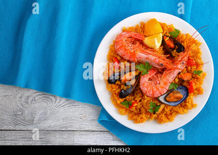 Porzione di pesce paella Valencia con gamberoni, cozze su gustosa crema di riso allo zafferano con spezie e spicchi di limone sulla piastra, vista da sopra Foto Stock