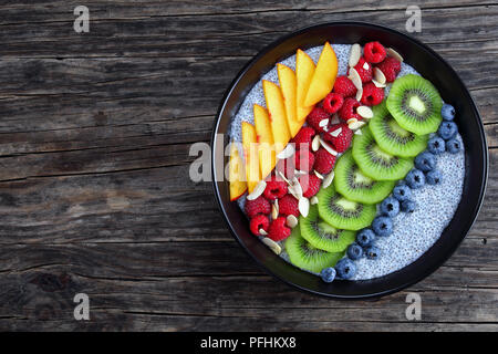 Sana colazione- deliziosa chia budino di semi con frutta fresca e bacche di colore nero ciotola sul vecchio tavolo in legno, orizzontale vista da sopra Foto Stock