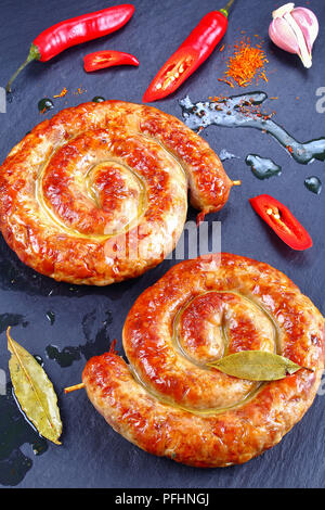 Delizioso caldo Bratwurst bavaresi - round salsicce fritte su spiedini di legno sul nero ardesia piastra con peperoncino e grasso bollente scende su sfondo, ver Foto Stock