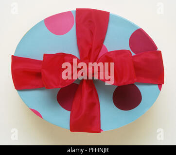 Un ovale Gift Wrapped in blue spotted carta e legate con un nastro rosso. Foto Stock